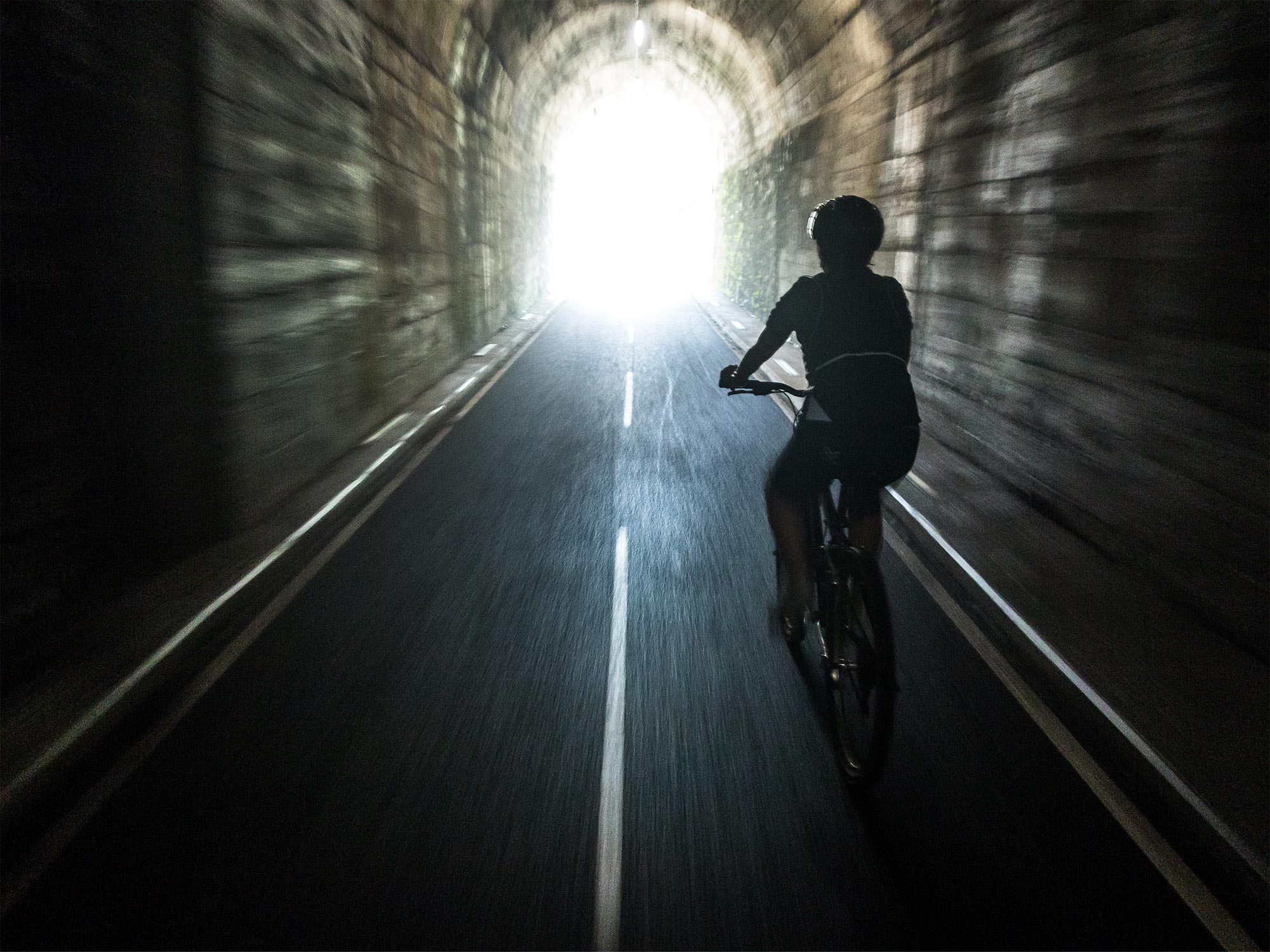 Un ciclista all’uscita dal tunnel della galleria lungo la ciclabile della valle Brembana ©Fabio Capelli, concorso fotografico TCI Italia in bicicletta