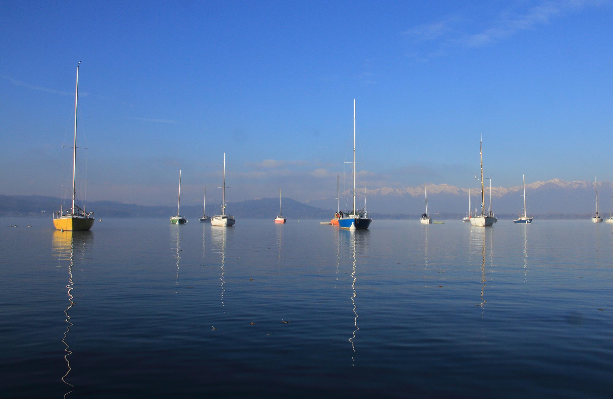 Le barche colorate sul Lago di Viverone: un vivace tocco di allegria che punteggia le acque serene, creando un suggestivo contrasto con il verde delle colline circostanti e il blu del cielo. © Tiziano Fogola