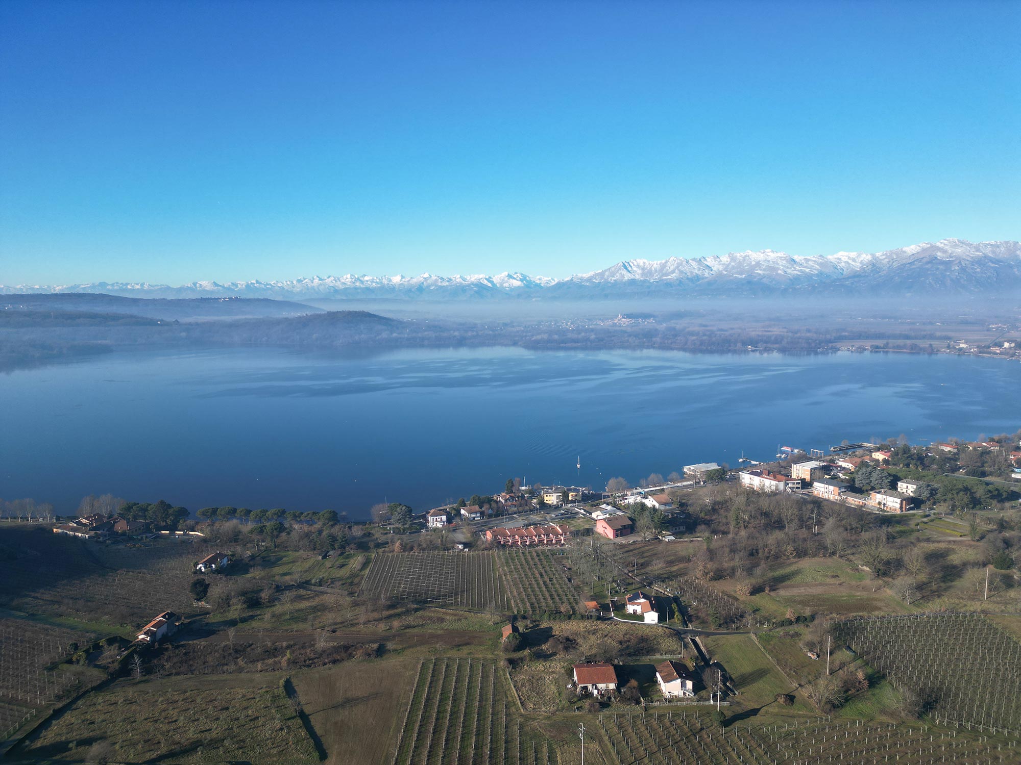 Il Lago di Viverone visto dall'alto: un'incantevole distesa di acque cristalline che riflettono il cielo, circondata da colline verdi e borghi pittoreschi, un panorama mozzafiato che incanta lo sguardo. © Valentina Avonda